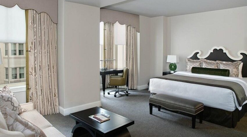 Elegantes Hotelzimmer mit Vorhängen, Bett, Schreibtisch und Sitzbank